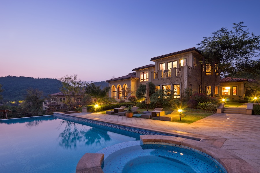 An outdoor pool in a luxurious backyard with outdoor lighting at dusk.